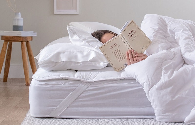 pessoa deitada em uma cama aconchegante enquanto lê um livro