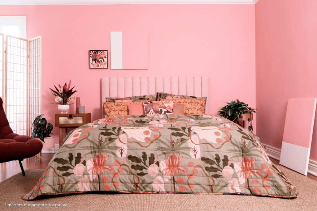 um quarto rosa inspirado no art déco. A cama possui uma estampa feita pela ilustradora em tons naturais e uma estampa orgânica. Ao fundo uma cabeceira rosa e dois vasos de plata, um em cada lado da cama. Há na parede dois quadros