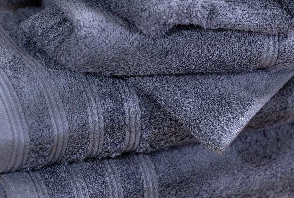 Na imagem estão toalhas de tom escuro, elas possuem textura macia, felpuda e estão dobradas umas sobre as outras.
