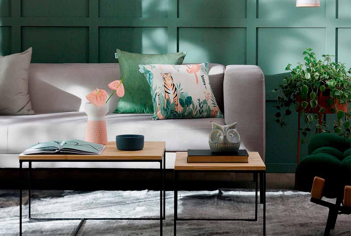 Sala decorada com sofá, almofadas, mesa de centro e plantas entre o sofá e a parede.